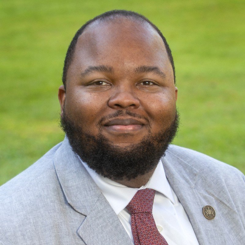 Dr. DeOnte Brown, Dean of Undergraduate Studies at Florida State University, smiling in a light gray suit and red tie.